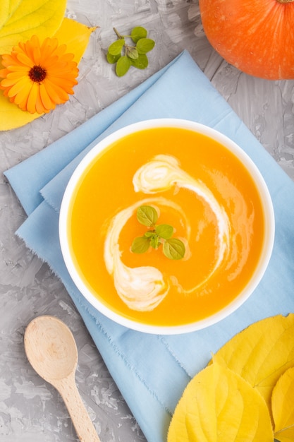 Traditionelle Kürbiscremesuppe mit in weißer Schüssel auf einer grauen Betonoberfläche mit blauer Serviette. Draufsicht, Nahaufnahme.