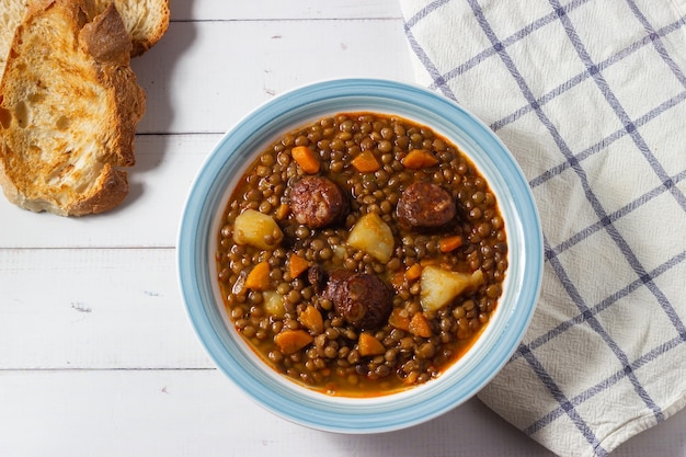 Traditionelle Linsensuppe mit Beinen, Karotten und Chorizo auf einem weißen und blauen Teller