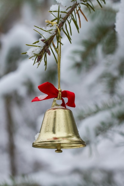 Foto traditionelle metallglocke mit rotem band auf dem schneebedeckten zweig eines immergrünen baumes