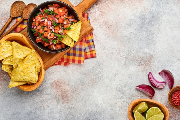 Traditionelle mexikanische Tomatensaucensalsa mit Nachos und Zutaten Tomaten, Chili, Knoblauch, Zwiebeln auf hellem Schiefersteinhintergrund. Konzept der lateinamerikanischen und mexikanischen Küche. Attrappe, Lehrmodell, Simulation.