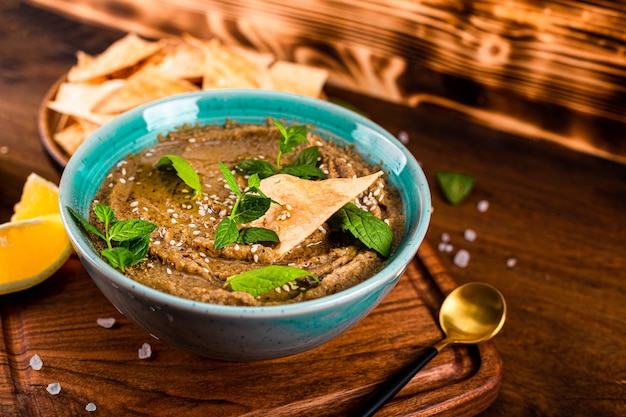 Traditionelle orientalische Vorspeise Baba Ganoush mit Sesam und Minzblättern Nahaufnahme. Auberginen-Hummus mit Pita-Chips auf dem Holztisch.