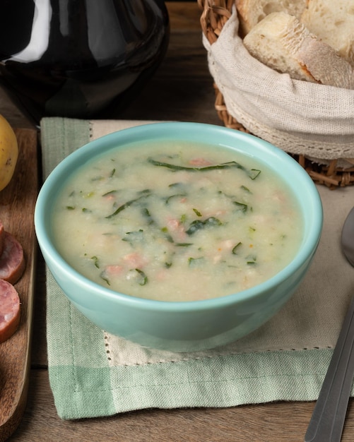 Traditionelle portugiesische grüne Suppe in einer Schüssel mit Brotscheiben und Wein über Holztisch