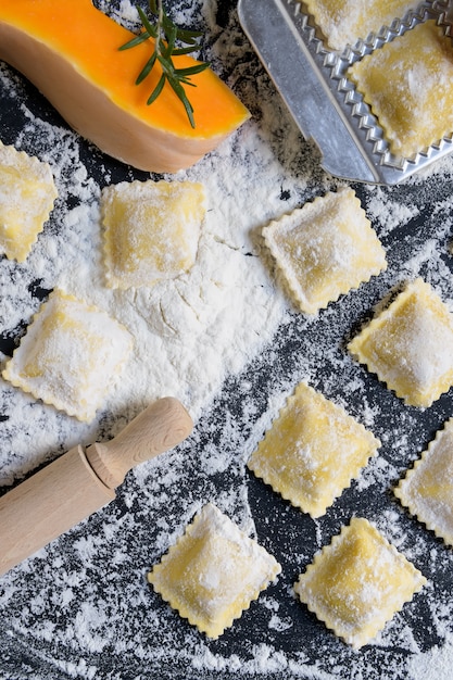 Traditionelle rohe Ravioli mit Kürbis auf einem Holztisch mit Mehl, handgemacht, Garprozess