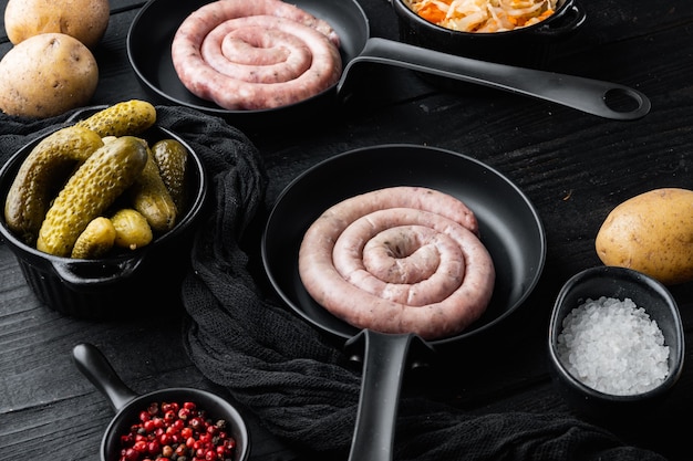 Traditionelle rohe spiralförmige Schweinewürste in einer gusseisernen Bratpfanne auf schwarzem Holztischhintergrund