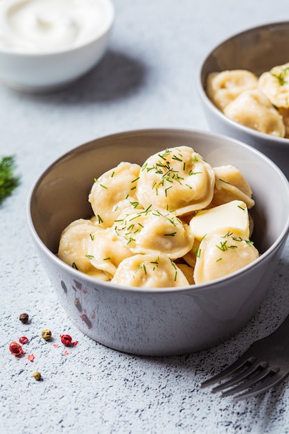 Traditionelle russische Fleischknödel mit saurer Sahne in der grauen Schüssel. Russisches Küchenkonzept.