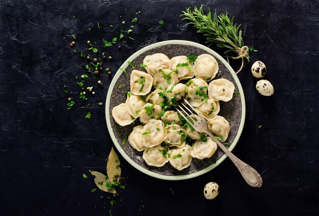 Foto traditionelle russische pelmeni-ravioli-knödel mit fleisch auf schwarzem betonhintergrund petersilie wachteleier pfeffer rosmarin lorbeerblatt und gewürze draufsicht copyspace