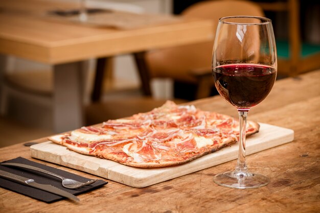 Traditionelle Schinken- und Brie-Käsepizza mit Glas Rotwein auf rustikalem Tisch