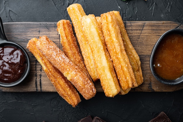 Foto traditionelle spanische dessert-churros mit zucker- und schokoladenset, auf schwarzem hintergrund, draufsicht flach gelegt