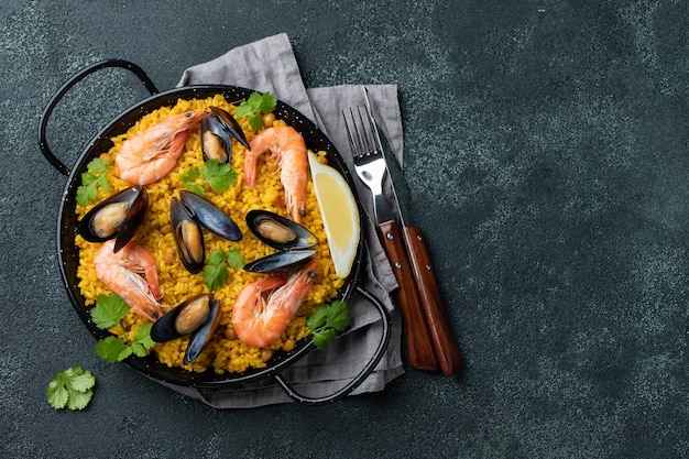 Traditionelle spanische Paella mit Meeresfrüchten in Pfanne mit Kichererbsen Garnelen Muscheln Tintenfisch auf schwarzem Betonbac...