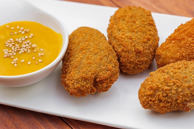 Traditionelle spanische Snack-Kroketten in Öl gebraten mit gelber Soße auf weißem Teller Seitenansicht auf Holz...