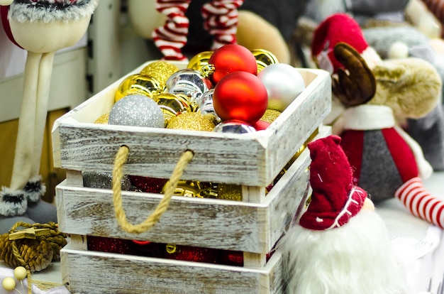 Traditionelle Spielzeugfiguren für Wohnkultur. Schachtel mit goldenen, silbernen und roten Glaskugeln auf dem Weihnachtsbaum für das neue Jahr.