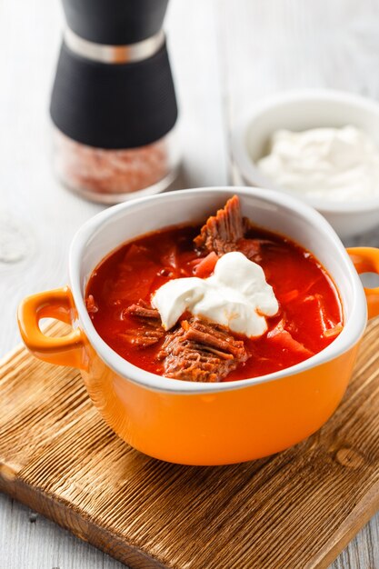 Traditionelle suppe der russischen und ukrainischen küche borschtsch. fleischsuppe mit rüben in einer orangefarbenen schüssel auf einem leichten holzbrett.