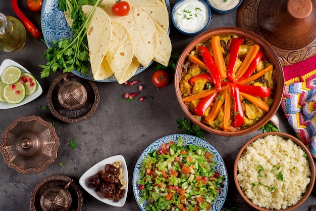 Traditionelle Tajine-Gerichte, Couscous und frischer Salat auf rustikalem Holztisch.