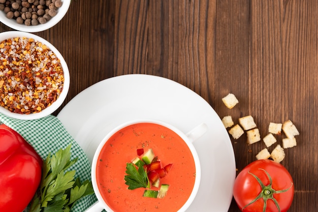 Traditionelle Tomatensuppe der Tomate auf einem hölzernen Hintergrund mit verschiedenen Gewürzen und Kräutern. Draufsicht.