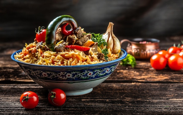 Traditionelle usbekische Mahlzeit namens Pilaw Reis mit Fleisch auf Teller mit orientalischem Ornament auf dunklem Holzhintergrund Langer Banner im Format Platz für Text