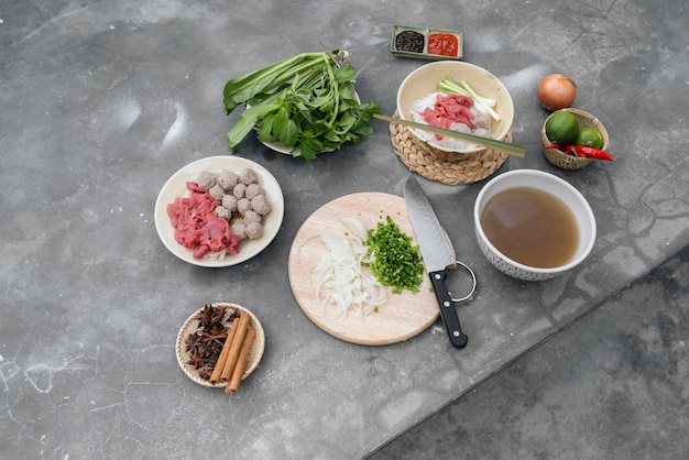 Traditionelle vietnamesische Suppe Pho Bo mit Kräutern, Fleisch, Reisnudeln, Brühe. Pho bo in Schüssel mit Stäbchen, Löffel. Platz für Text. Ansicht von oben. Asiatische Suppe Pho bo auf Holztischhintergrund. Vietnamesische Suppe