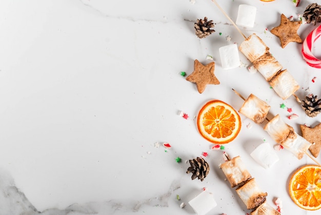 Traditionelle Weihnachtsbonbonzuckerstange, Eibisch, getrocknete Orange, Lebkuchensterne, gebacken auf Feuereibischaufsteckspindeln auf weißem Marmor, Draufsicht copyspace