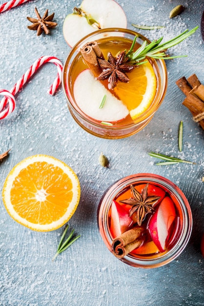 Traditionelle Wintergetränke, Weiß- und Rotglühweincocktail, mit Weiß- und Rotwein, Gewürzen, Apfel, Orange. Auf einem hellblauen Tisch