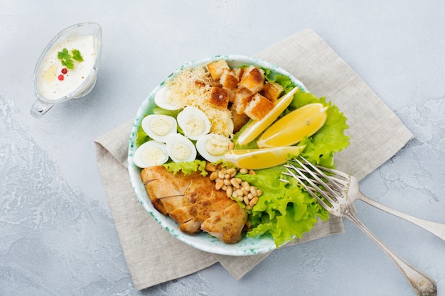 Traditioneller Caesar-Salat mit Wachteleiern und Pinienkernen in einer leichten Keramikschale Auf einer grauen Stein- oder Betonoberfläche. Lunch Bowl. Selektiver Fokus. Draufsicht.