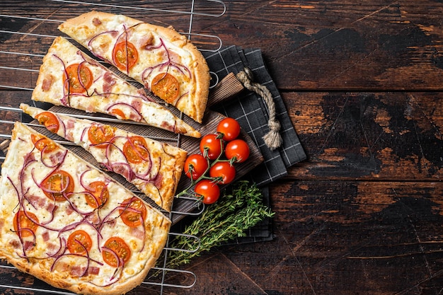 Traditioneller deutscher Flammkuchen oder Flammkuchen mit Frischkäse, Speck, Tomaten und Zwiebeln. Hölzerner Hintergrund. Ansicht von oben. Platz kopieren.