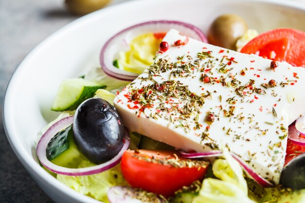 Traditioneller griechischer Salat mit Feta, Oliven, Tomate und Gurke in einem weißen Teller.