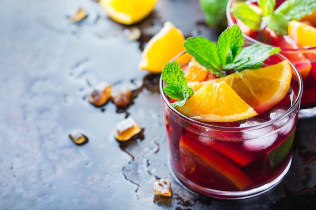 Traditioneller kalter spanischer Sangria-Cocktail mit Rotwein und Zutaten auf einem schwarzen Tisch Zitrusfrüchte orange Limette Zitrone Minzblätter und Eis für heiße Sommertage Kopieren Sie den Hintergrund des Raums