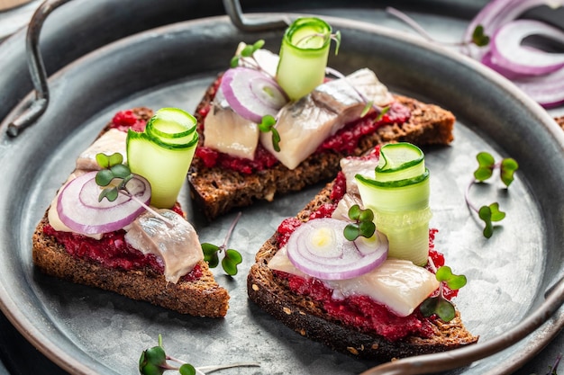 Traditioneller Matjes mit Rote-Bete-Salat, frischen Gurken und Zwiebelringen auf Roggenbrot-Toast skandinavische Küche