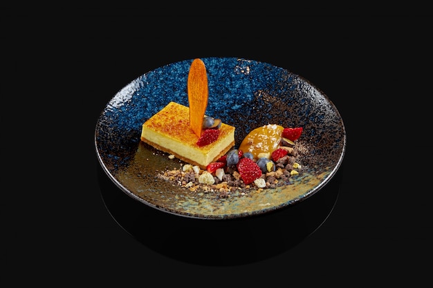 Traditioneller New Yorker Käsekuchen mit Blaubeeren, Erdbeeren und karamellisierter Birne in einer schwarzen Keramikplatte. Stilvolles Restaurant servieren. Dessert serviert