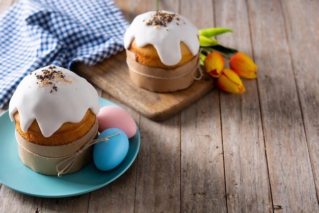 Traditioneller Osterkuchen, bunte Eier und Tulpen auf Holztisch.