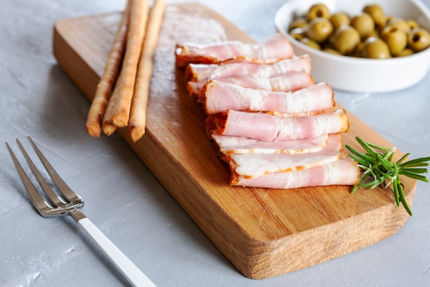 Traditioneller Pancetta-Speck, serviert mit eingelegten Oliven und Grissini-Brot