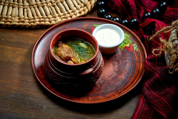 Traditioneller ukrainischer grüner Borschtsch mit Fleisch und Sauerrahm in einem Tontopf