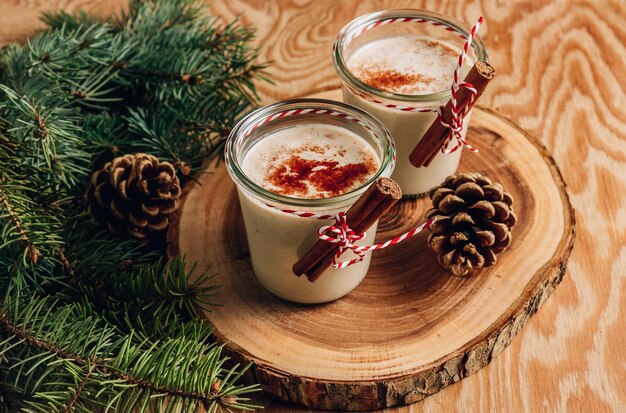 Foto traditioneller weihnachtlicher milchcocktail eierlikör mit zimt serviert in zwei gläsern auf festlichem holztisch selektiver fokus