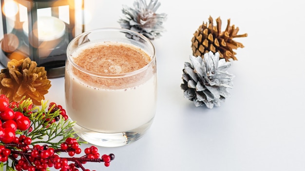 Traditioneller Weihnachtscocktail Eierlikör mit Eiern, Alkohol, geriebener Muskatnuss und Zimt Nahaufnahme. Süßes traditionelles Getränk für Weihnachten und Winter auf dem Tisch mit roten Dekorationen und goldenen Tannenzapfen