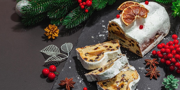 Traditioneller Weihnachtsstollen, deutscher Kuchen, europäisches Gebäck, duftendes selbstgebackenes Brot mit Gewürzen und Trockenfrüchten, Weihnachtsbaumzweige und Dekorationen, schwarzer Hintergrund, Bannerformat