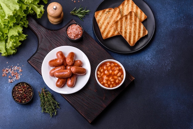 Traditionelles englisches Frühstück mit Eiern, Toast, Würstchen, Bohnen, Gewürzen und Kräutern auf einer grauen Keramikplatte