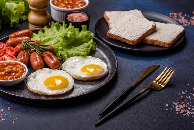 Traditionelles englisches Frühstück mit Eiern, Toast, Würstchen, Bohnen, Gewürzen und Kräutern auf einer grauen Keramikplatte