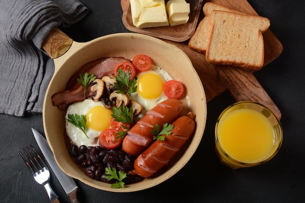 Traditionelles englisches Frühstück mit Speck, Spiegeleiern, Würstchen, gebackenen Bohnen, Pilzen