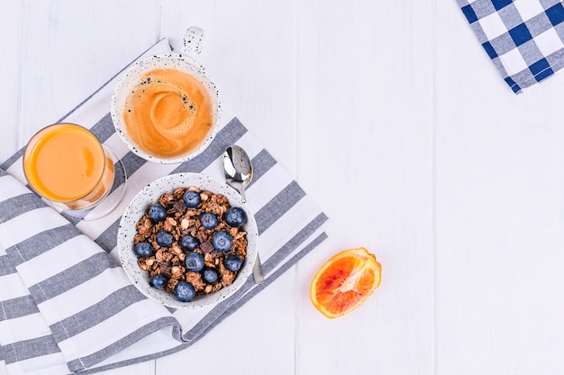 Traditionelles europäisches Frühstück auf weißem hölzernem Hintergrund. Müsli mit Beeren, Kaffee und Orangensaft. Flach liegen. Kopieren Sie Platz