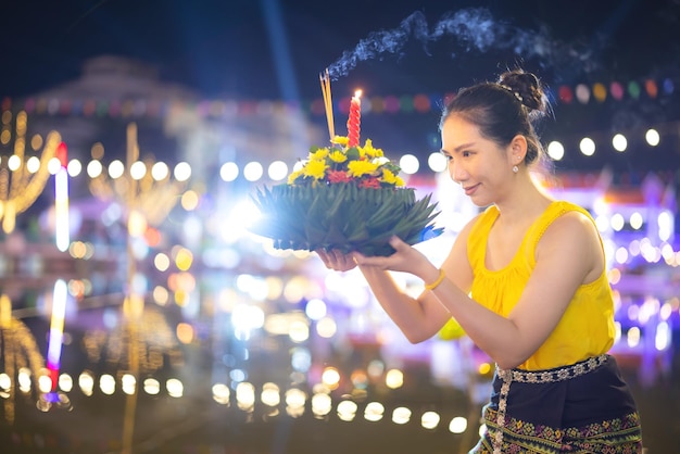 Traditionelles Fest von Loy Krathong Eine schöne Thailänderin hält in einer Vollmondnacht bei Loy Krathong-Feierlichkeiten in Thailand eine Krathong-Zierform aus Bananenblättern