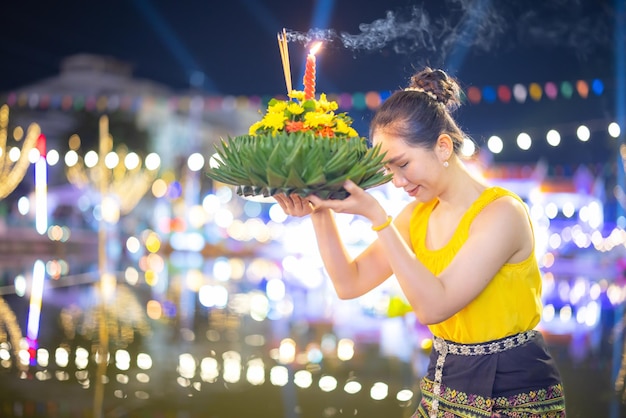 Traditionelles Fest von Loy Krathong Eine schöne Thailänderin hält in einer Vollmondnacht bei Loy Krathong-Feierlichkeiten in Thailand eine Krathong-Zierform aus Bananenblättern