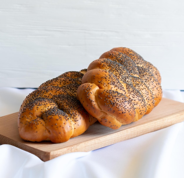 Traditionelles frisch gebackenes jüdisches Gebäck Zwei hausgemachte Challas mit Mohn auf Holzbrett Seitenansicht weißer Hintergrund