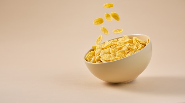 Traditionelles Frühstück mit fallenden Cornflakes in einer Schüssel isoliert auf beigem Hintergrund