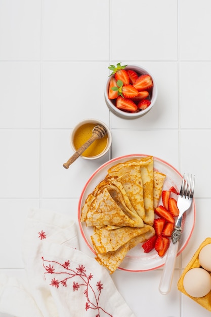 Traditionelles Gericht für den Urlaub Maslenitsa. Dünne Crepes Pfannkuchen mit Honig, frischen Erdbeeren und Zutaten für das Frühstück. Draufsicht.