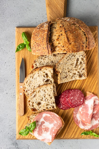 Traditionelles Handwerkerbrot mit Samen und Schweinswurst und Salami diente auf einem hölzernen Schneidebrett. Offenes Sandwich mit Schweinefleischwurst.