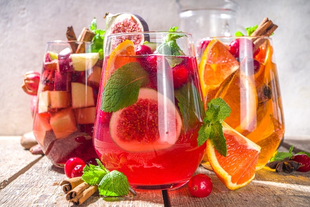 Traditionelles Herbstwintergetränk heiße würzige Sangria - rot, rosa, weiß. Mit Apfelwein, rosa Rotwein, Äpfeln, Orangen, Granatapfel, Preiselbeere, Pflaume, Feigen, Zimtstangen. Rustikaler Holztisch mit Kopienraum