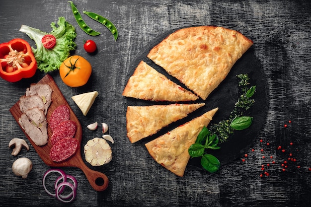 Traditionelles italienisches Pizza calzone mit Bestandteilen auf einem Stein und einem dunklen hölzernen verkratzten Hintergrund