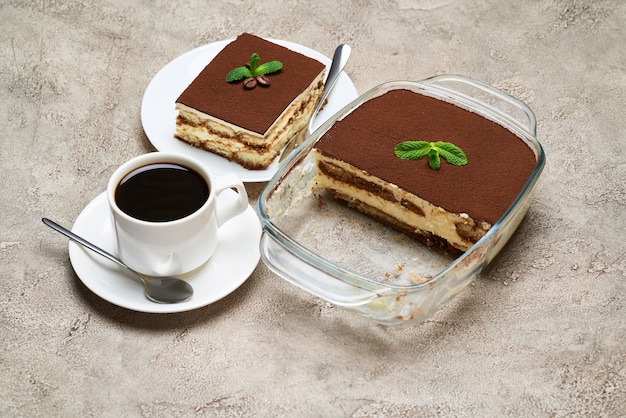 Traditionelles italienisches Tiramisu-Dessert in Glasbackform und Portion auf grauem Betontisch