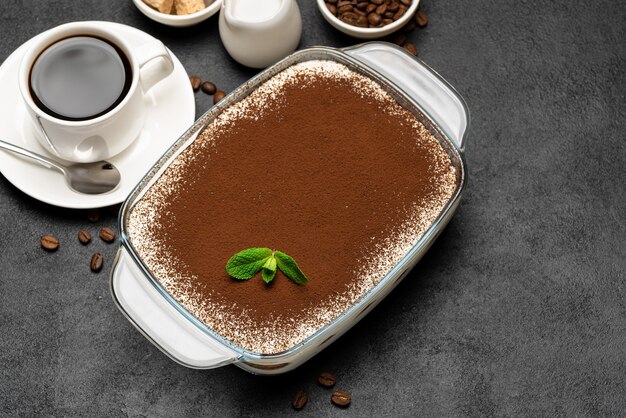 Traditionelles italienisches Tiramisu-Dessert in Glasbackform und Tasse frischen heißen Espressokaffee auf Betonhintergrund oder -tisch