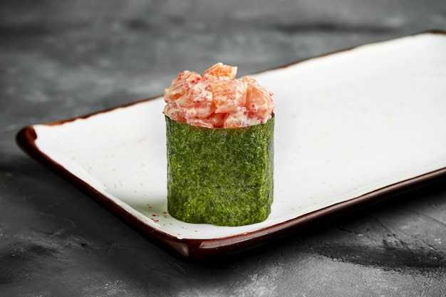 Traditionelles japanisches Gunkan-Sushi mit Lachs, Kaviar und würziger Sauce in Nori auf einem weißen Teller. Nahaufnahme, selektiver Fokus