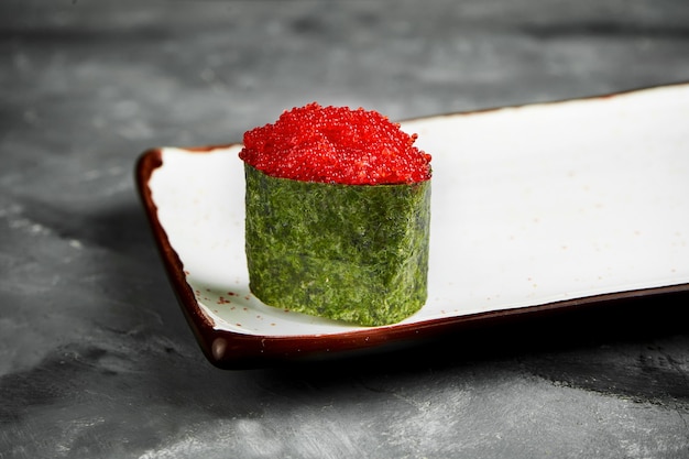 Traditionelles japanisches Gunkan-Sushi mit Tobiko-Kaviar und würziger Sauce in Nori auf einem weißen Teller. Nahaufnahme, selektiver Fokus